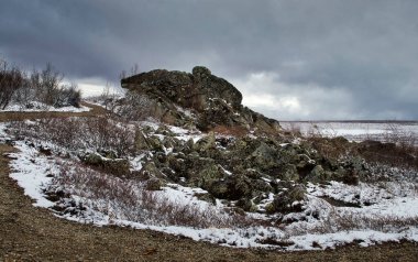 Alaska 'da karanlık, bulutlu bir bahar gününde Dalton Otoyolu' nda yürüyüş yolunun yanında kayalar var.. 