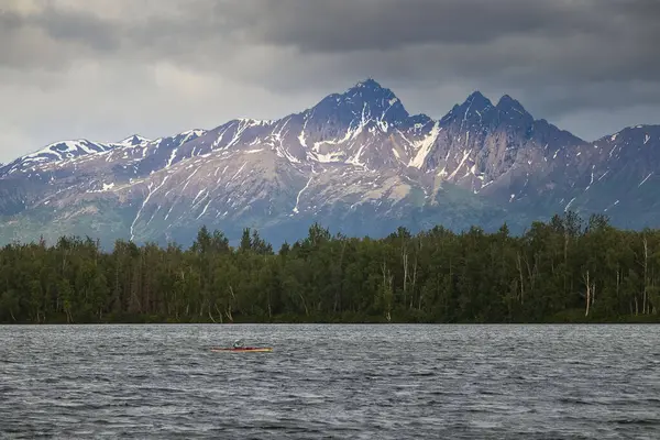 Wasilla, Alaska - 26 Haziran 2023: Wasilla, Alaska 'da bulutlu bir yaz gecesinde Lucille Gölü' nün arkasındaki dağlarda güneş.