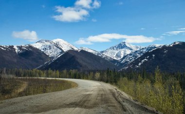 Alaska 'da güneşli bir bahar gününde arka planda dağlar olan Dirt Dalton Otoyolu. 