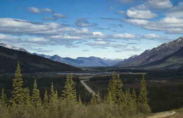 Alaska 'da güneşli bir bahar gününde Dalton Highway dağların arasından geçiyor.. 