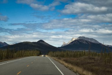 Alaska 'da güneşli bir bahar gününde Dalton Otoyolu' nda ağaçlar ve dağlarla kaplı bir manzara.. 