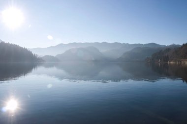 Bled, Slovenya - 16 Ocak 2022: Slovenya 'da sisli bir kış gününde Bled Gölü üzerinde mavi gökyüzünde parlak güneş.