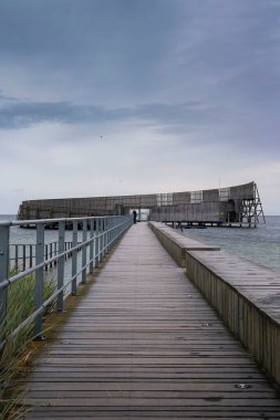 Kastrup, Danimarka - 12 Ekim 2019: Danimarka 'da bulutlu bir sonbahar gününde, deniz suyu havuzu etrafında dairesel bir yapı olan Kastrup Sobad' a giden tahta yol.