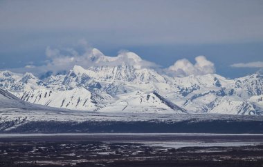 Alaska 'da güneşli bir bahar gününde, eriyen karla kaplı, karlı dağlar ve beyaz bulutlar..