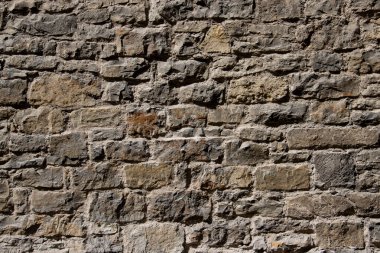 Bu görüntü, parlak güneş ışığı altında aydınlatılan antik bir dokusu ve doğal toprak tonuyla taştan bir duvar yakalıyor. Tarih, mimari ve doğal manzara elementleri kavramları için mükemmel..