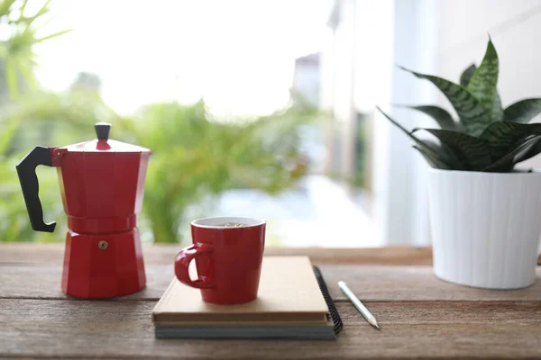 Red coffee and red moka pot and notebook on brown wooden table outdoor