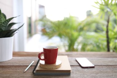 Kırmızı kahve, kırmızı telefon ve dışarıdaki kahverengi ahşap masada bulunan defterler.