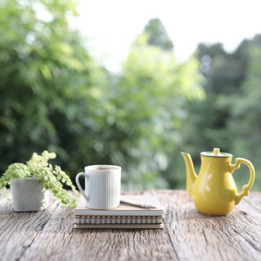 Beyaz çay fincanı ve sarı antika çay demliği ve küçük bitkiler ahşap masada.