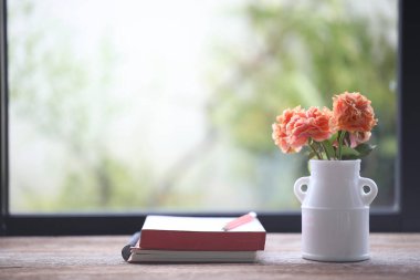 Açık pencerelerin önünde turuncu güller ve defterler.