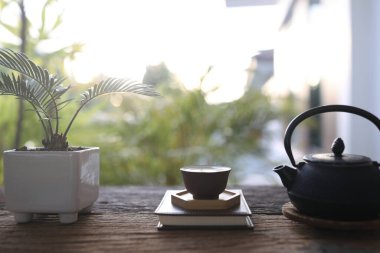 Metal tea pot and tea cup and plant pot on wooden table balcony outdoor