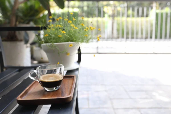 ブラックベンチにコーヒーグラスカップとイエローデイジーフラワーポット — ストック写真