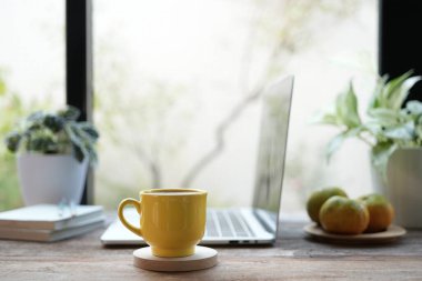Sarı kahve fincanı, dizüstü bilgisayar ve beyaz çiçekler evden beyaz masa içinde çalışıyor.