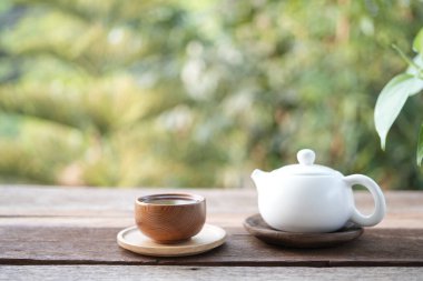 Beyaz çay fincanı ve çaydanlık ve ahşap tepside ve yeşil arka planlı balkon manzaralı.