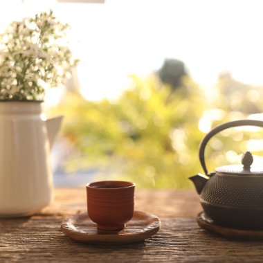 Tea cup and black metal tea pot and flowers on wooden table