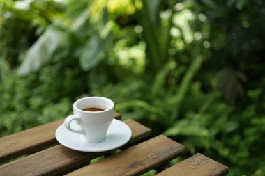 Beyaz kahve fincanı yeşil yemyeşil arkaplanlı ahşap masada.