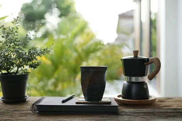 stock image Tall black coffee mug and moka pot and notebook diary on old brown wooden table