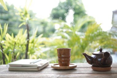 Toprak takımı çaydanlığı, ahşap çay fincanı ve ahşap masaya dizilmiş defterler.