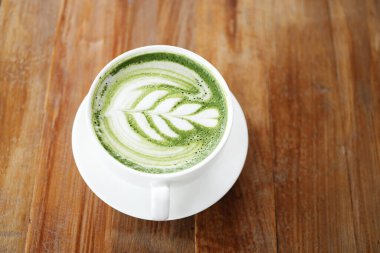 Kahverengi ahşap masa yüzeyinde latte sanatıyla yeşil çay