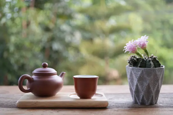 stock image Earthenware teapot and tea cup and pink cactus flower on wooden table