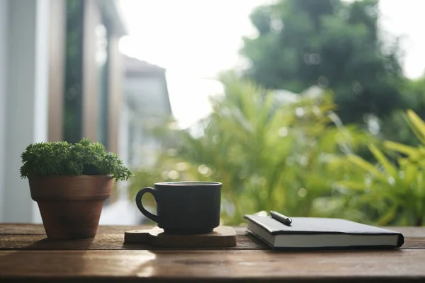 Black coffee cup and notebook and plant pot on table at outdoor