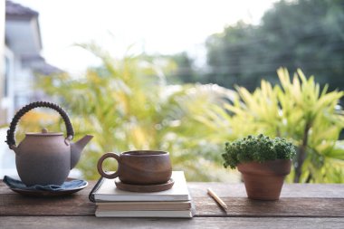 Kahverengi çay fincanı ve çaydanlık ile kahverengi saksı ve defterler.