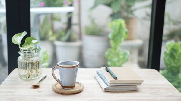 Ceramic white coffee cup and notebook and with plant pot on wooden table
