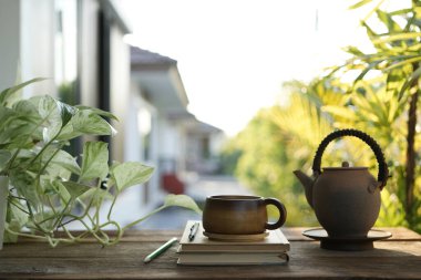 Çay fincanı ve çömlek çaydanlığı balkonda ve dizüstü bilgisayar manzarasında.