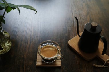 Koyu kahverengi ahşap masada, cam bir fincanda kahve.