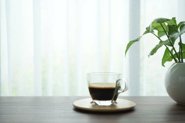 kahve fincanı ve saksı pencere manzaralı ahşap masa üzerinde.