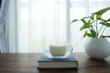 Not defterine bir bardak süt ve pencere manzaralı ahşap masaya saksı.