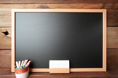 Ahşap duvarda renkli tebeşirler ve silgi olan siyah karatahta.