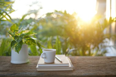 Beyaz bardak, defter ve kalem güneş ışığı altında, ahşap masada.