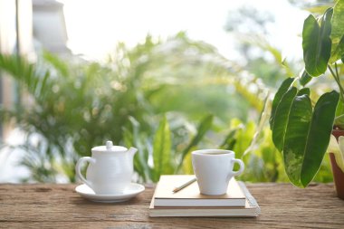 Çaydanlık ve çay fincanı. Defterleri var. Açık hava bahçesinde içiyorlar.