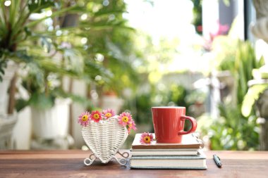 Kırmızı kahve fincanı ve pembe çiçek ahşap masada beyaz kalp sepetinde.