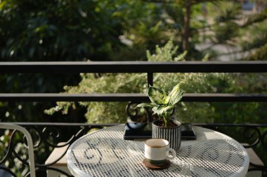 Samimi balkon çalışma alanı, beyaz kahve fincanı ve güneş ışığında tablet.