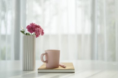 Pembe bardak ve gül, beyaz perdeli pencere kenarında, rahat çalışma alanı