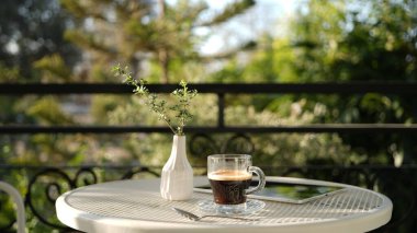 Açık hava balkonunda beyaz metal masa üzerinde not defterleri olan kahve bardağı.