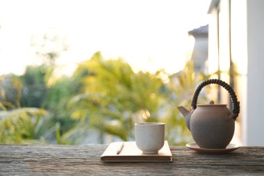 Antika çay demliği, çay fincanı ve defter, rahat balkon çalışma alanı.
