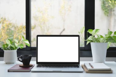Beyaz ekranlı dizüstü bilgisayar, kahve ve pencere kenarındaki bitkiler.