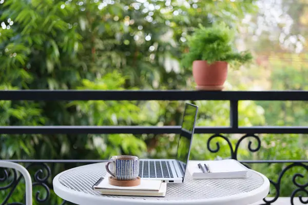 Öğleden sonra çay molası, beyaz metal bir masada dizüstü bilgisayarla, balkon manzaralı.