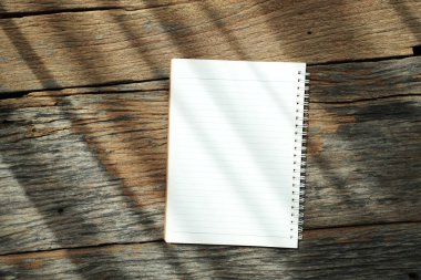 Güneş ışığı altında eski ahşap masa üzerinde yüzük klasörlü beyaz defter