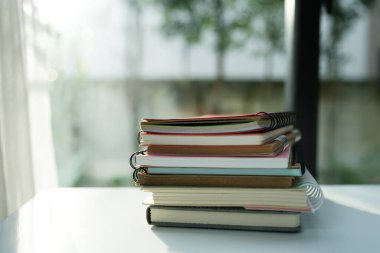Pencerenin yanındaki beyaz masada eski defterler yığını