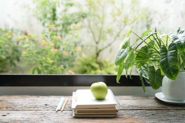 Elma dizüstü bilgisayar yığını ve saksı bitkisi pencere önündeki ahşap masa üzerinde, yazmak için rahatlatıcı sahne