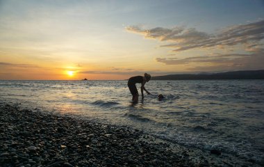 Gün doğumunda evcil köpeklerle sahilde oynayan bir kadın..