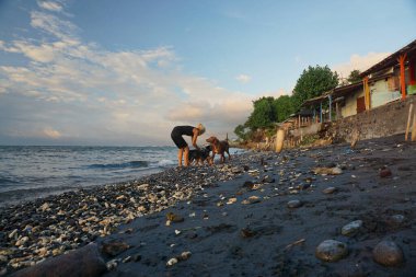 Gün doğumunda evcil köpeklerle sahilde oynayan bir kadın..