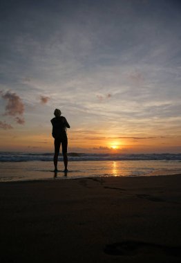 Güzel bir gün batımını görmek için sahilde duran bir kadın..