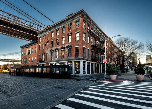 stock image Brooklyn, NY - USA - March 26, 2023 Sunrise view of red brick buildings on the corner of Old Fulton Street and Water Street, under the Brooklyn Bridge.