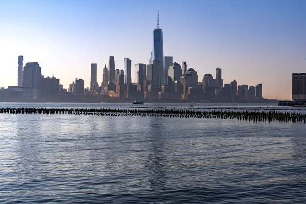 New York, New York - ABD - 7 Eylül 2023 Hudson Nehri 'nin karşısındaki Lower Manhattan' ın gündoğumu manzarası. İskelenin kalıntıları ve ön planda bir feribot..