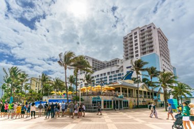 Hollywood Plajı, FL - ABD - 9 Şubat 2024 Tahta kaldırımda yürüyen üç turist manzarası ikonik Margaritaville Plaj Tatil Köyü 'nün önünden geçti..