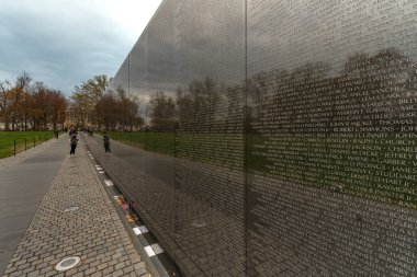 Washington DC - ABD - 23 Mart 2024 Vietnam Gaziler Anıtı 'nı ziyaret eden turistler. Maya Lin tarafından tasarlanmış siyah granit duvarlar. Ölen ya da kaybolan askerlerin isimleriyle kazınmış.